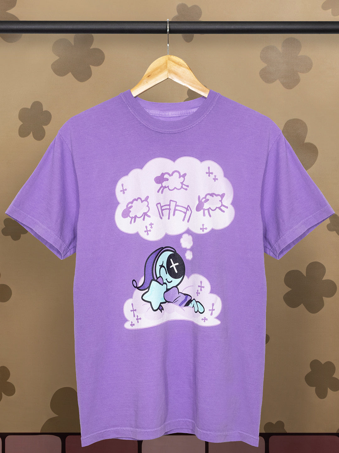 Purple t-shirt with a graphic design on a hanger against a patterned wall.