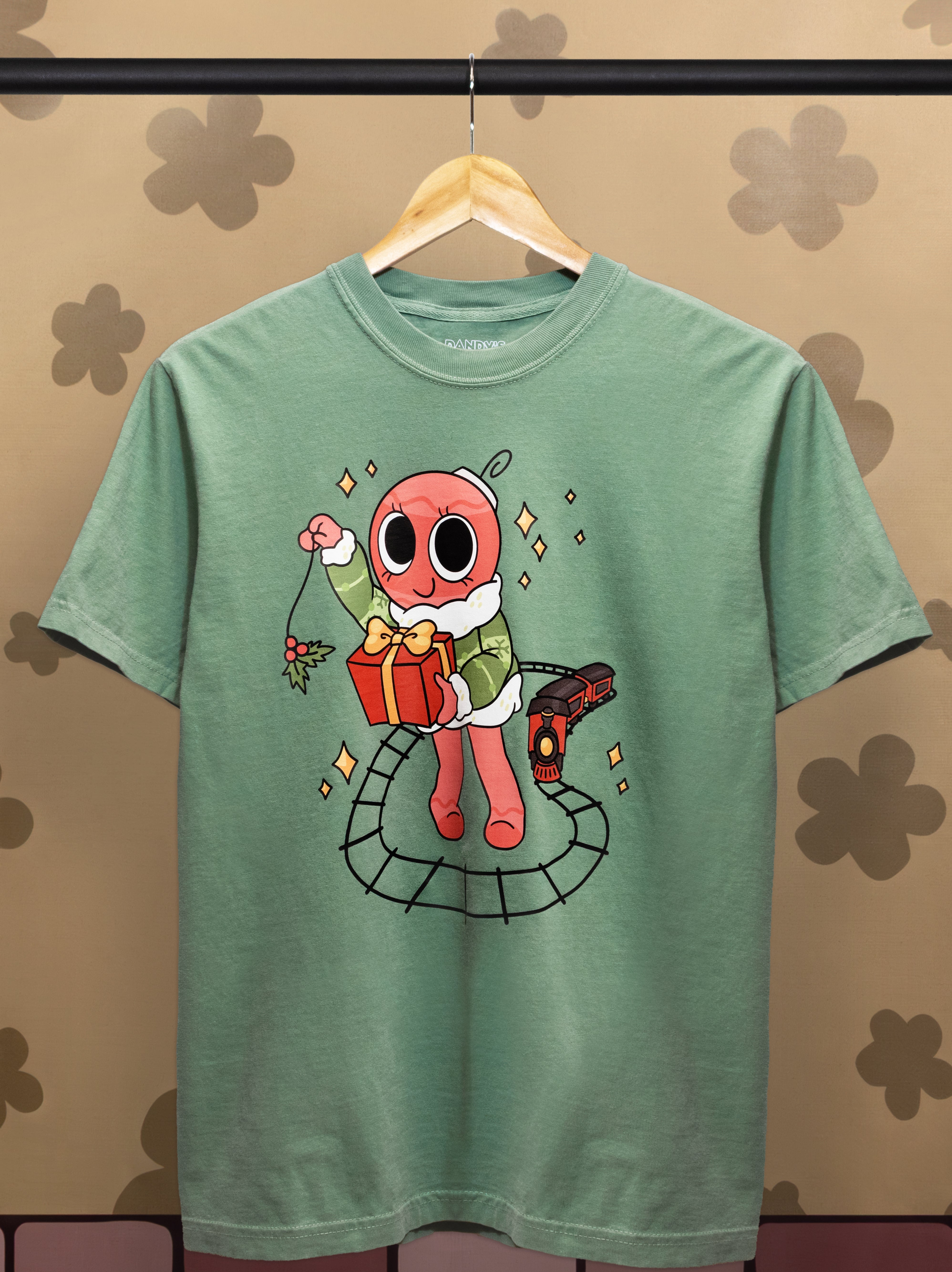 Green t-shirt with a cartoon character holding a gift on a hanger against a patterned wall.