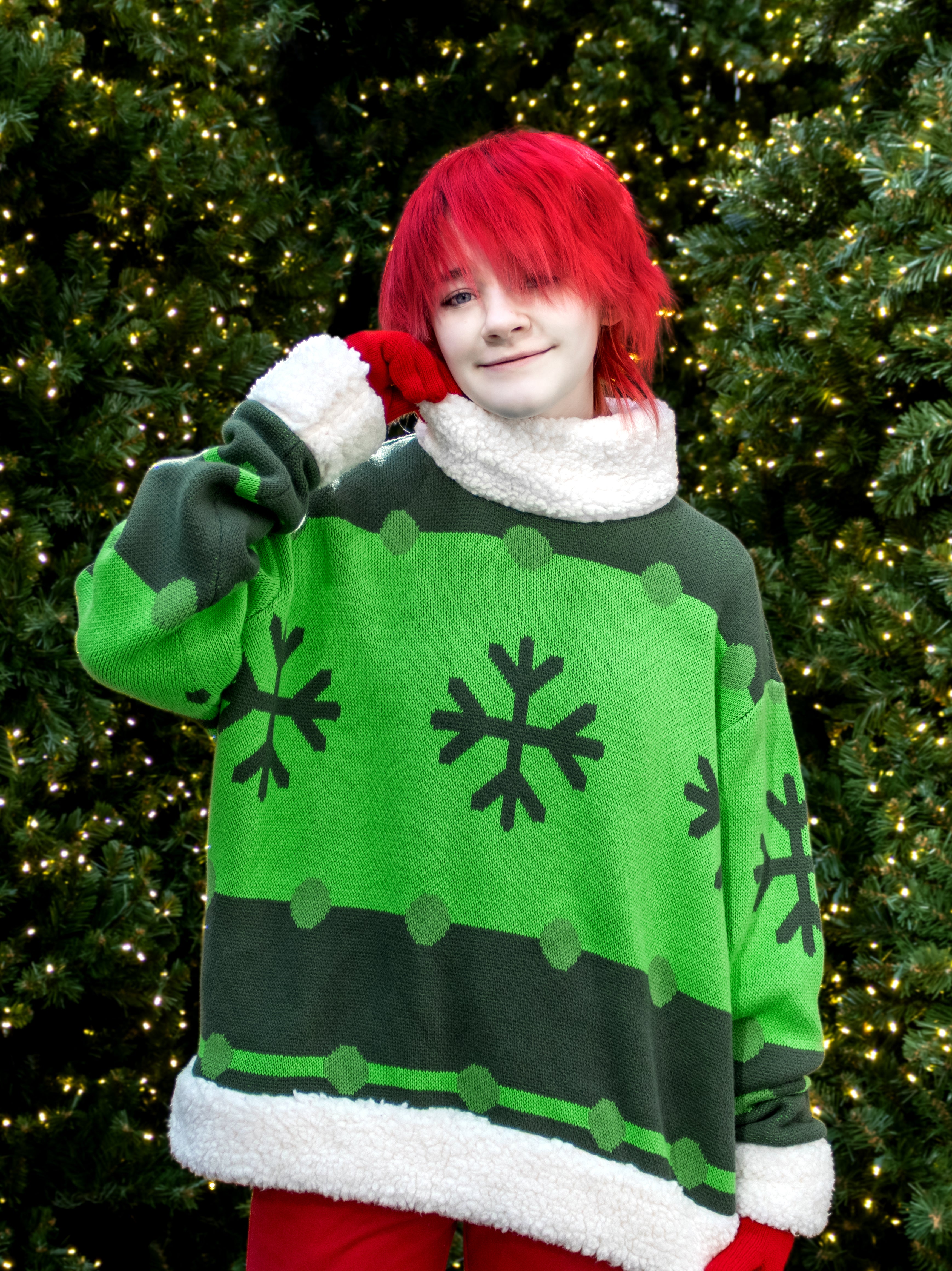 Person wearing a green and black snowflake sweater in front of a decorated Christmas tree.