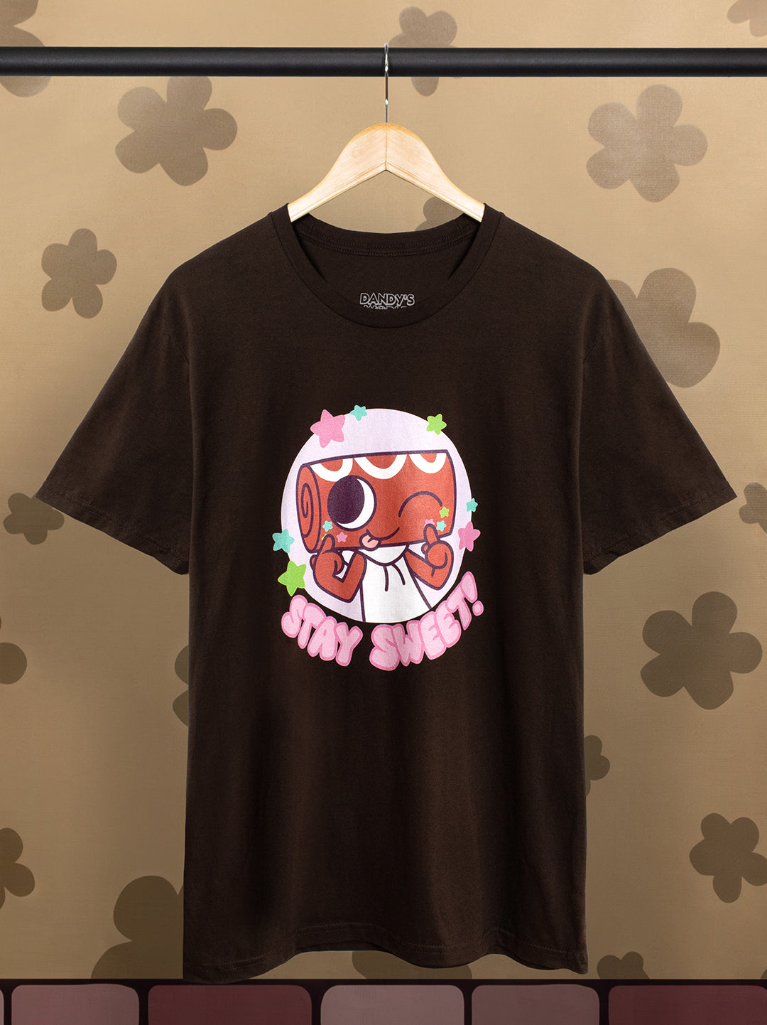t-shirt of cosmo winking and smiling inside a circle with stars. text: stay sweet! on hanger with flower background