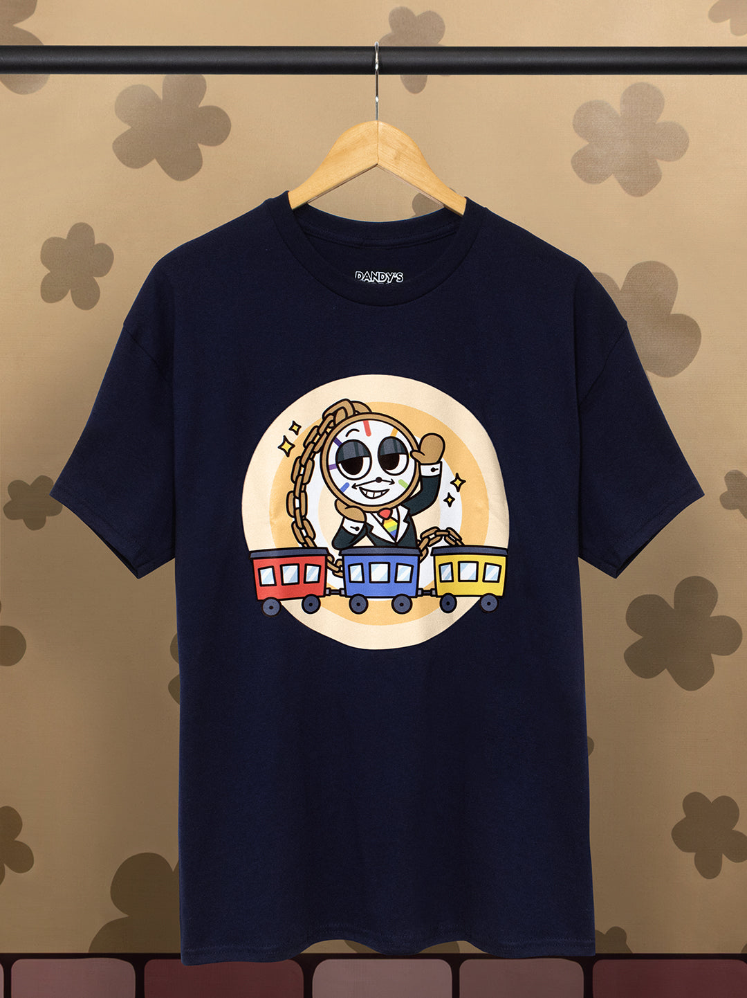 Navy blue t-shirt with a cartoon character and train design on a hanger against a patterned wall.