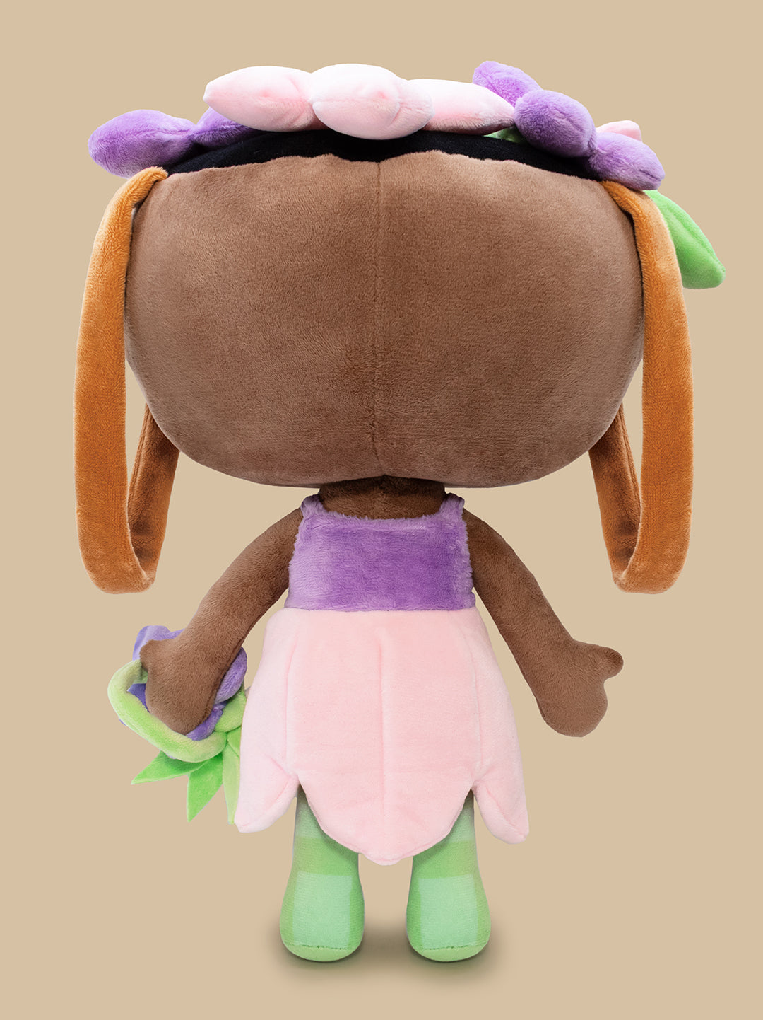 Plush toy with a brown body, purple top, pink skirt, and green legs on a beige background