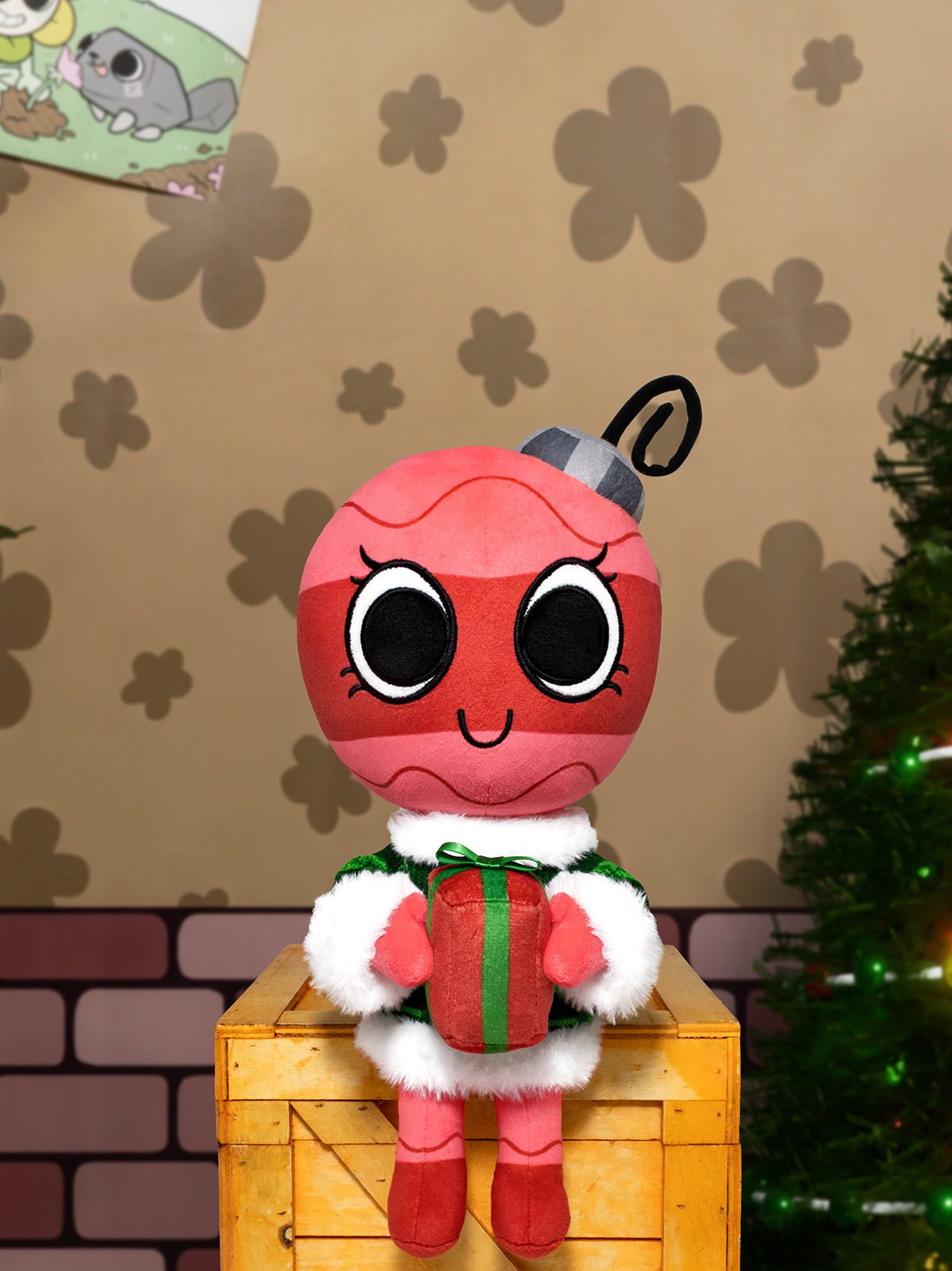Plush toy with a red face and sweater sitting on a wooden crate with a Christmas tree in the background.