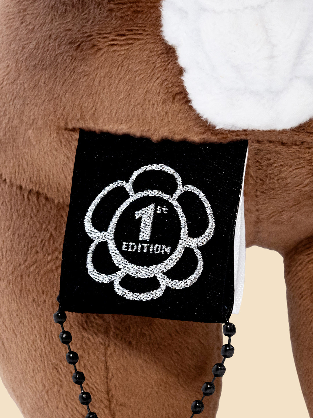 Plush toy with a '1st Edition' patch on a beige background