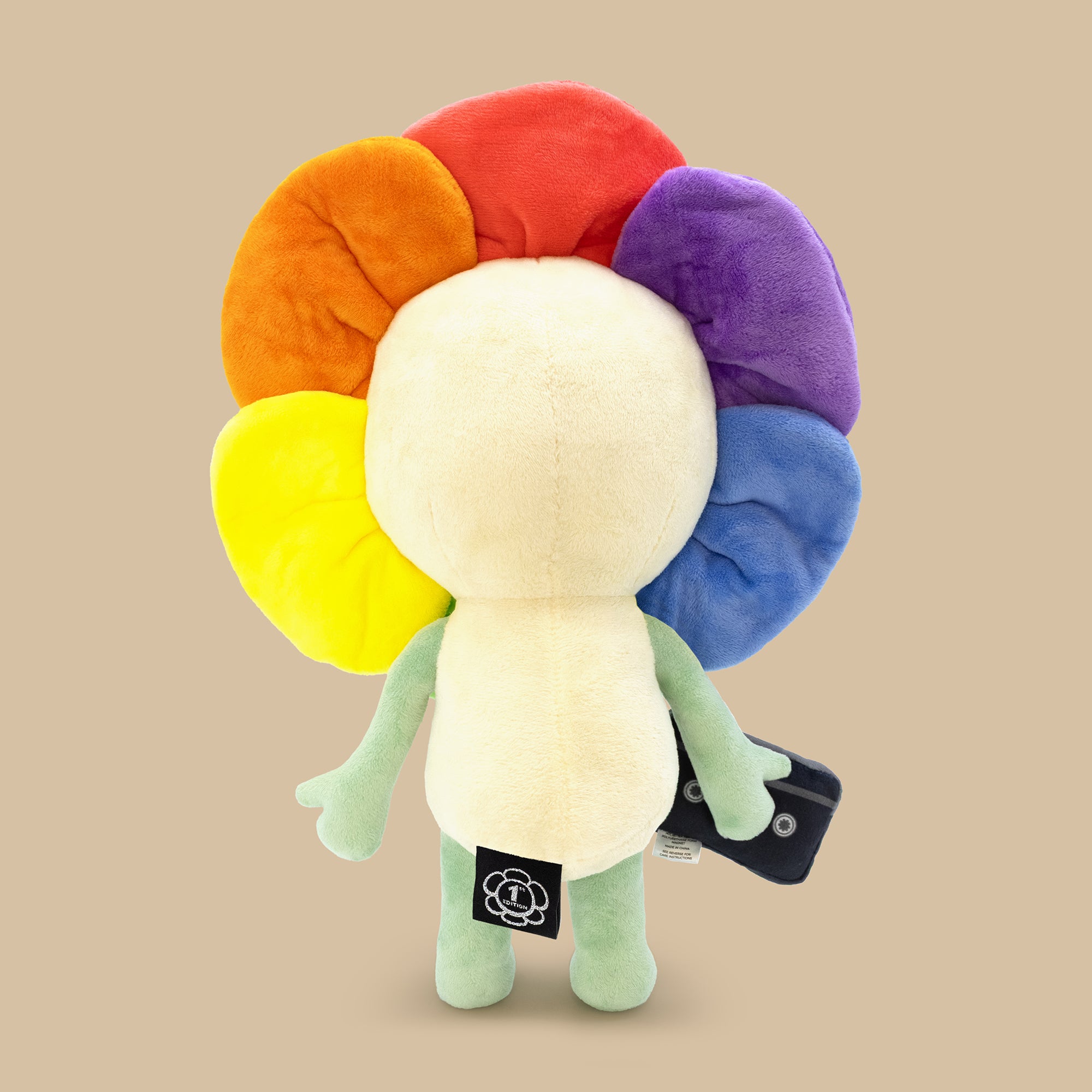 Plush toy with rainbow-colored head on a beige background with 1st edition tag on bottom
