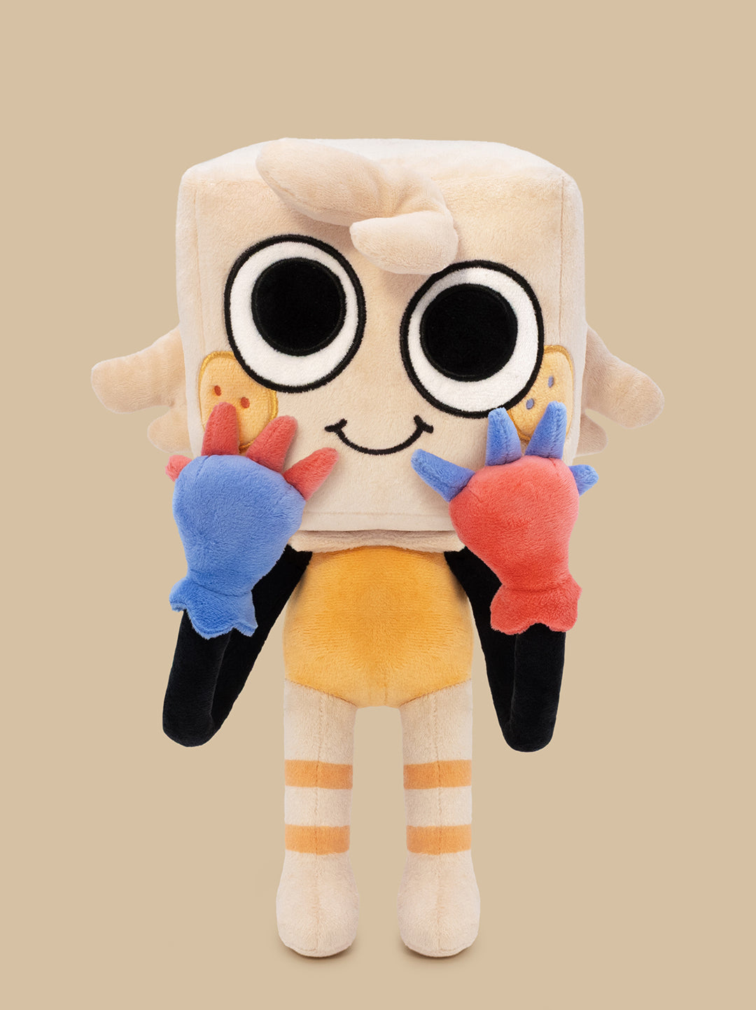 A plush toy character with a cream-colored square head, large black-and-white eyes, a small smile, yellow shorts, striped cream and orange legs, and colorful blue, red, and black hands, shown against a plain beige background.