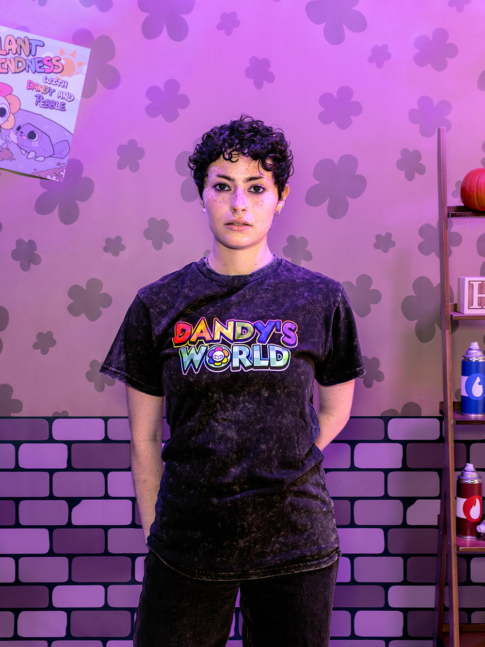 Person wearing a 'DANDY'S WORLD' t-shirt in front of a purple floral and brick-patterned wall.