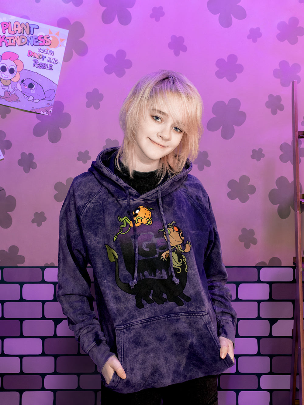 Person wearing a hoodie with cartoon characters in front of a purple floral and brick wall.