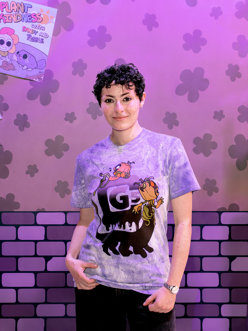Person wearing a t-shirt with a graphic design in front of a purple floral and brick wall background