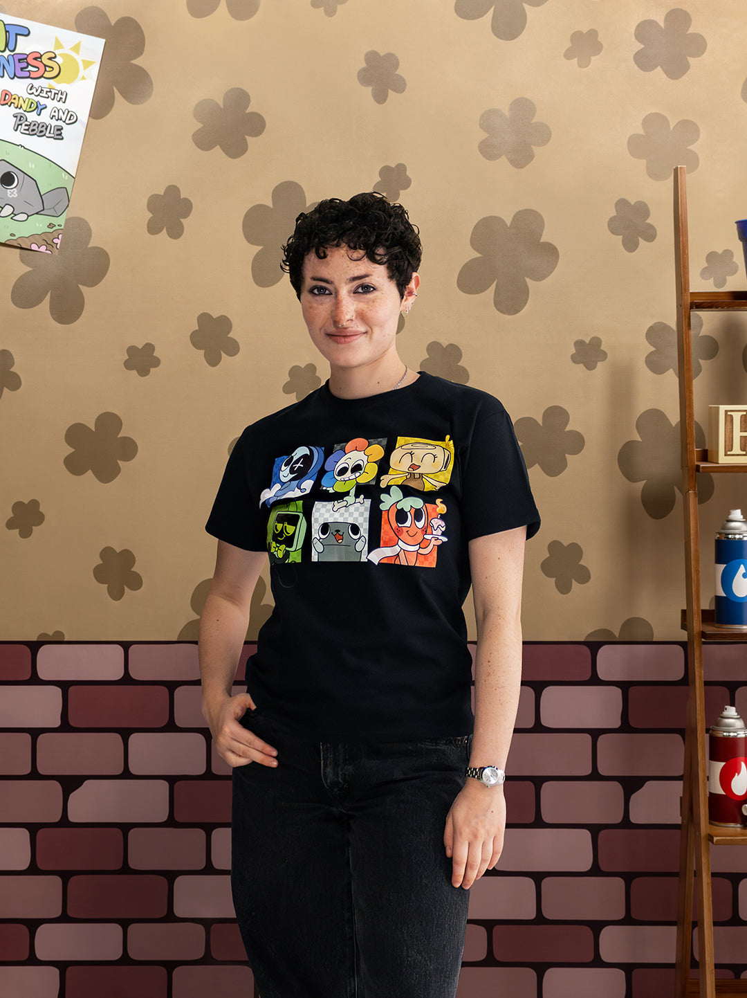 Person wearing a black t-shirt with colorful graphic design against a patterned wall.