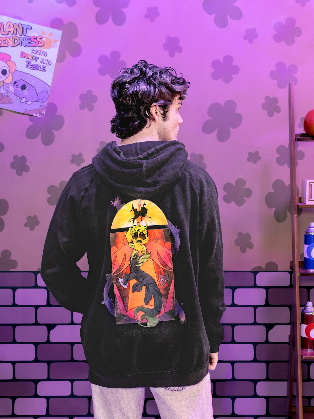 Person wearing a black hoodie with a colorful graphic on the back against a purple brick wall.
