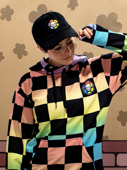 Person wearing a colorful checkered hoodie and cap with a logo on a patterned background