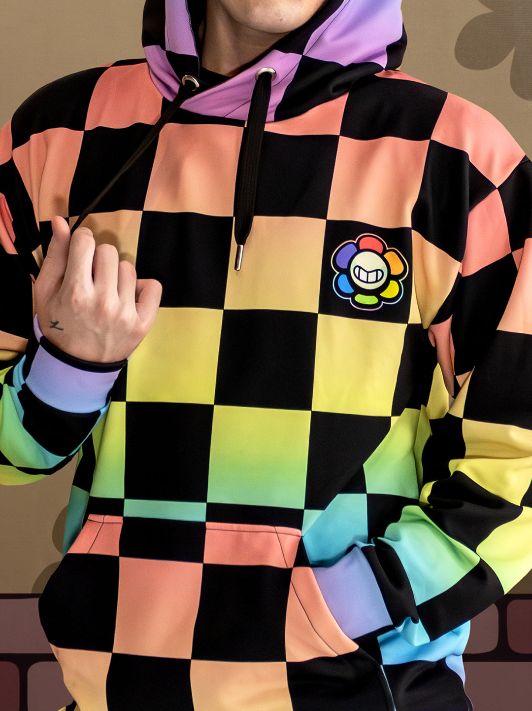 Person wearing a colorful checkered hoodie with a logo on a plain background