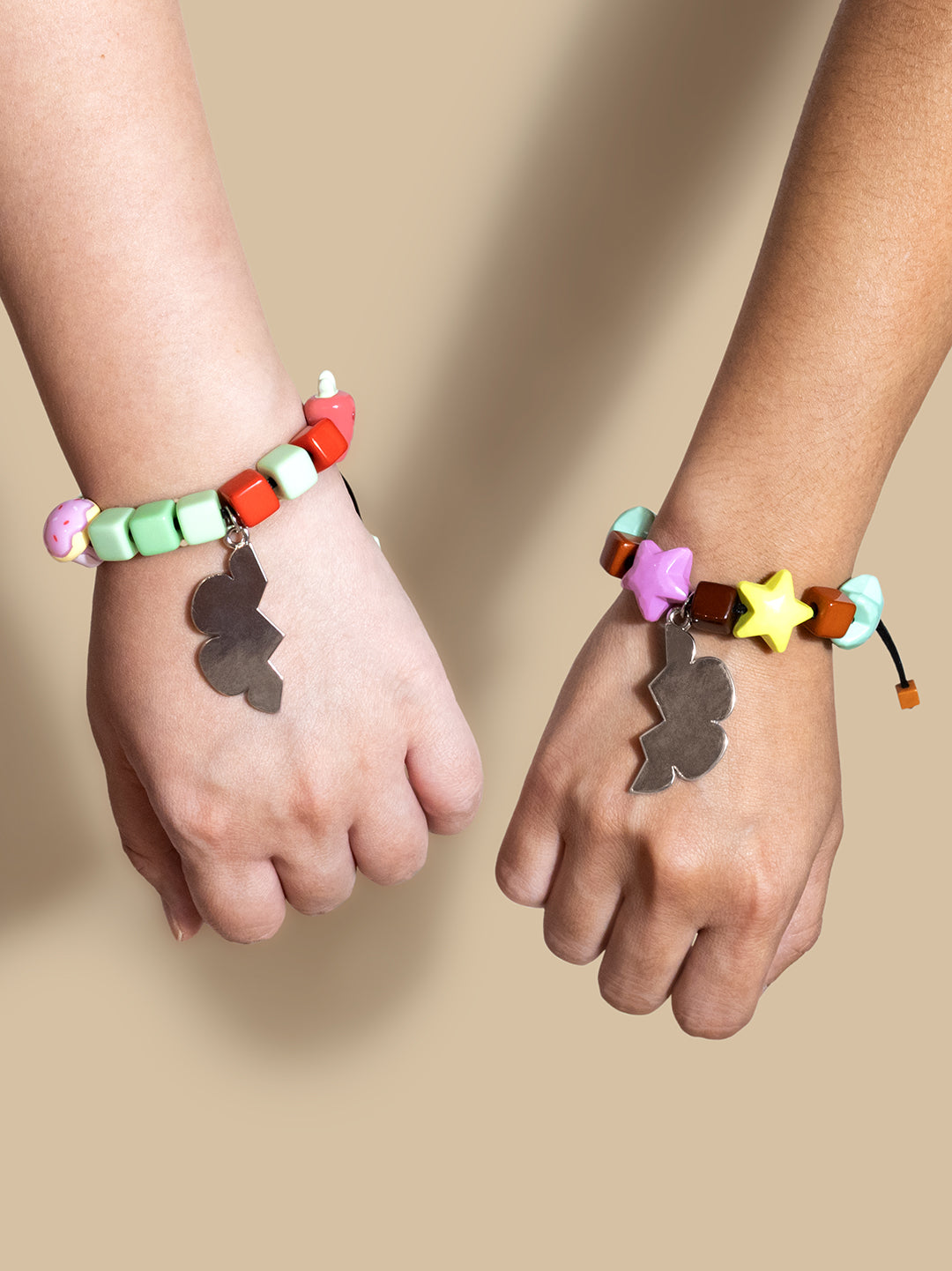 Two hands wearing colorful beaded bracelets with metallic cloud-shaped charms, set against a solid beige background.