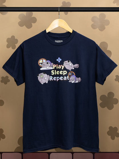 Navy blue t-shirt with 'Play Sleep Repeat' graphic on a hanger against a floral-patterned wall.