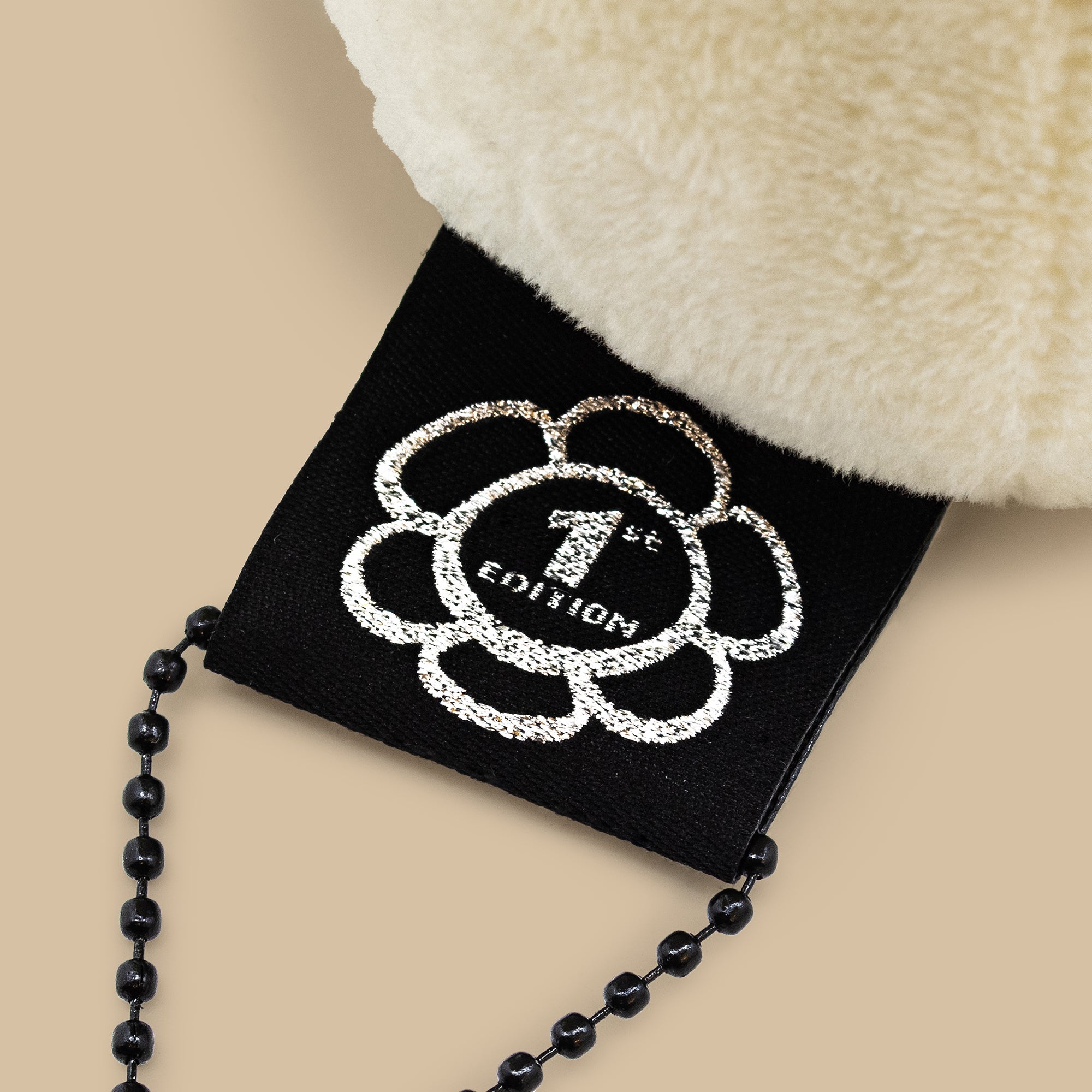 Black beaded chain on a black card with '1st Edition' design, against a beige background.