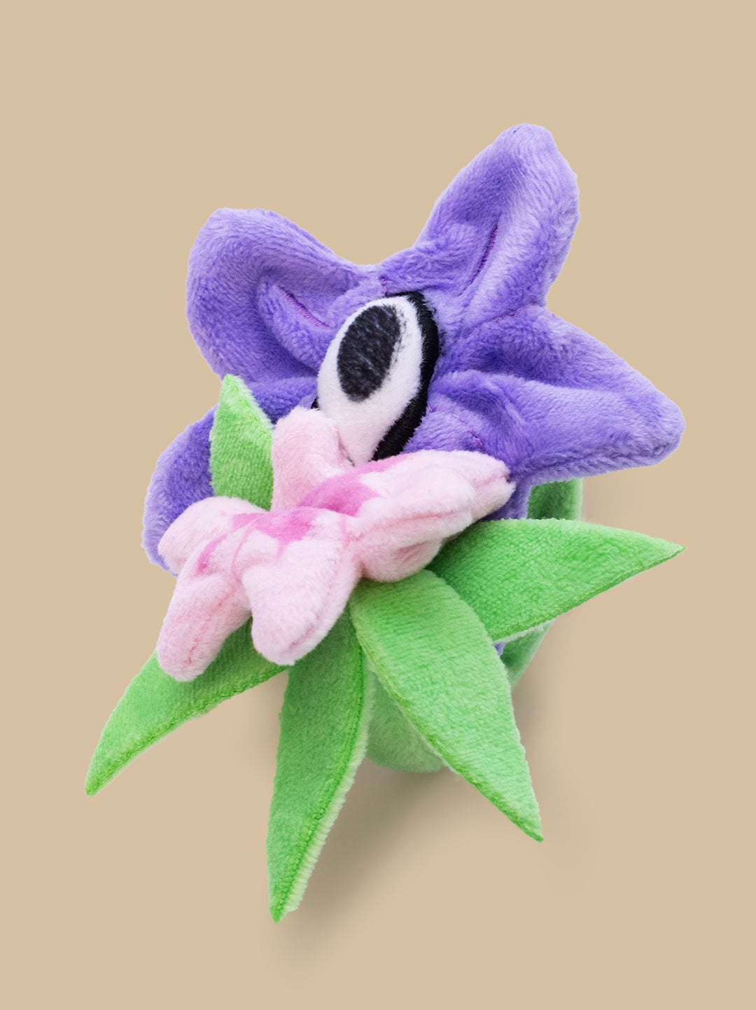 Plush toy shaped like a purple flower with green leaves on a beige background