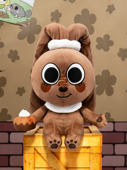 Plush toy resembling a cartoon character with a brown body and white accents, sitting on a wooden crate against a patterned wall.