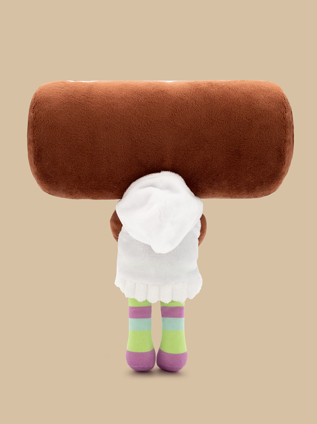 A plush doll viewed from behind, wearing a white hoodie and colorful striped socks. The background is a solid warm beige studio backdrop.