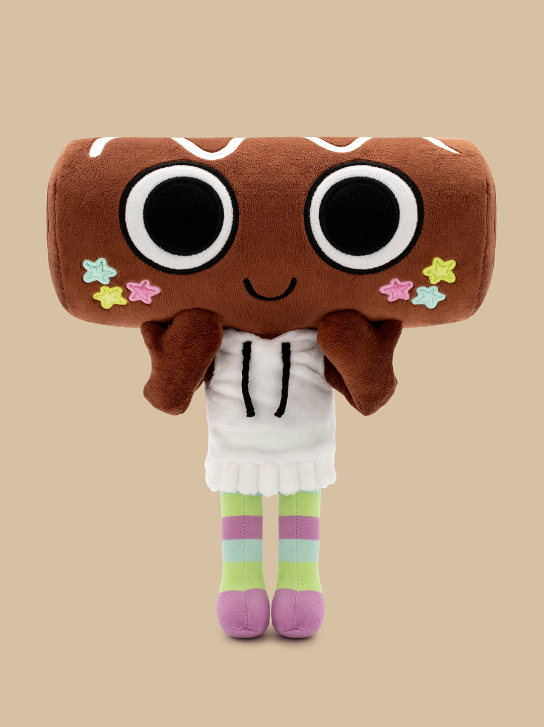A plush toy shaped like a brown donut or cookie with large black-and-white eyes, a small smile, colorful star accents, a white dress, and striped pastel legs, centered on a plain beige background.