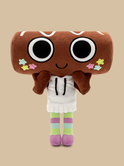 A plush toy shaped like a brown donut or cookie with large black-and-white eyes, a small smile, colorful star accents, a white dress, and striped pastel legs, centered on a plain beige background.