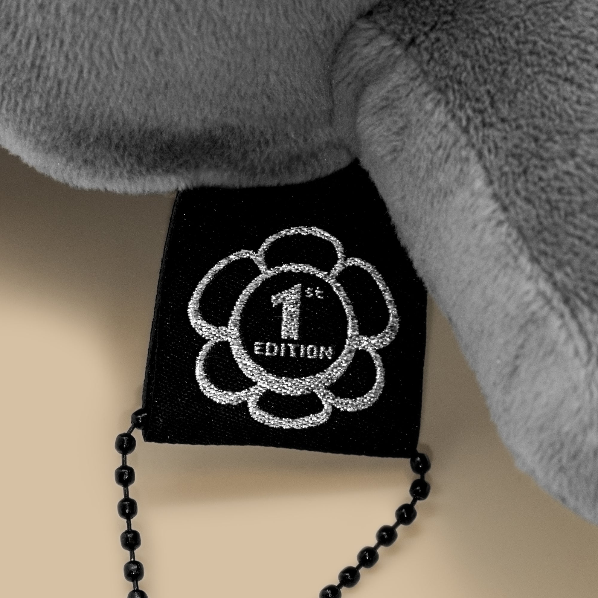 Black box with '1st Edition' design and black beaded chain on a neutral background