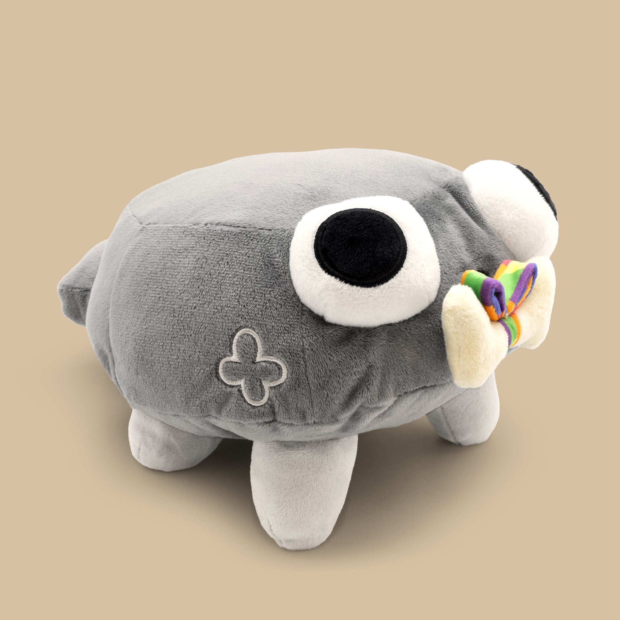 Gray plush toy with a large eye and rainbow bow on a beige background