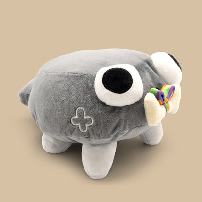 Gray plush toy with a large eye and rainbow bow on a beige background