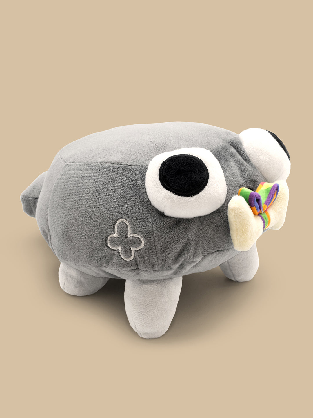 Gray plush toy with a large eye and rainbow bow on a beige background
