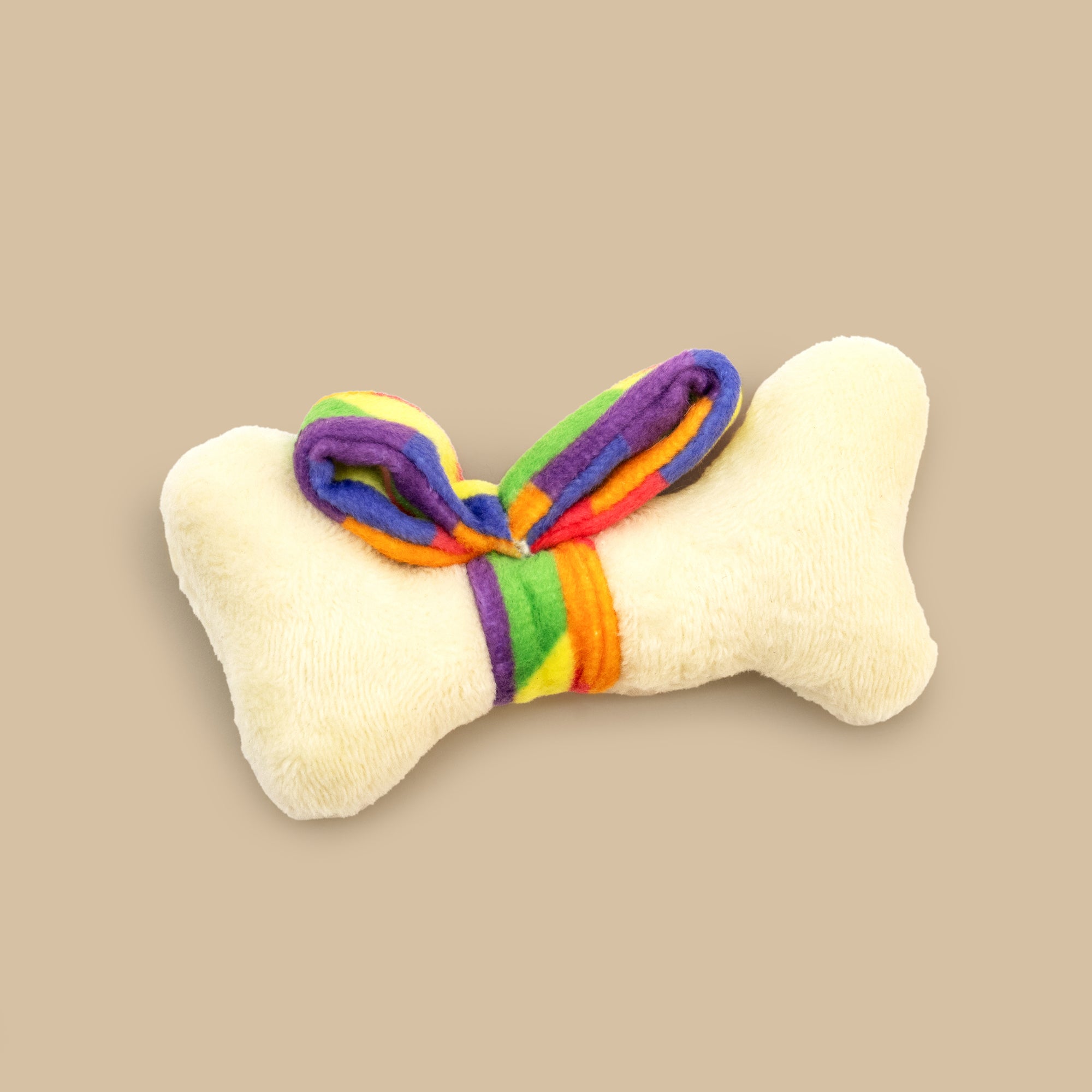 Bone-shaped toy with rainbow bow on a beige background