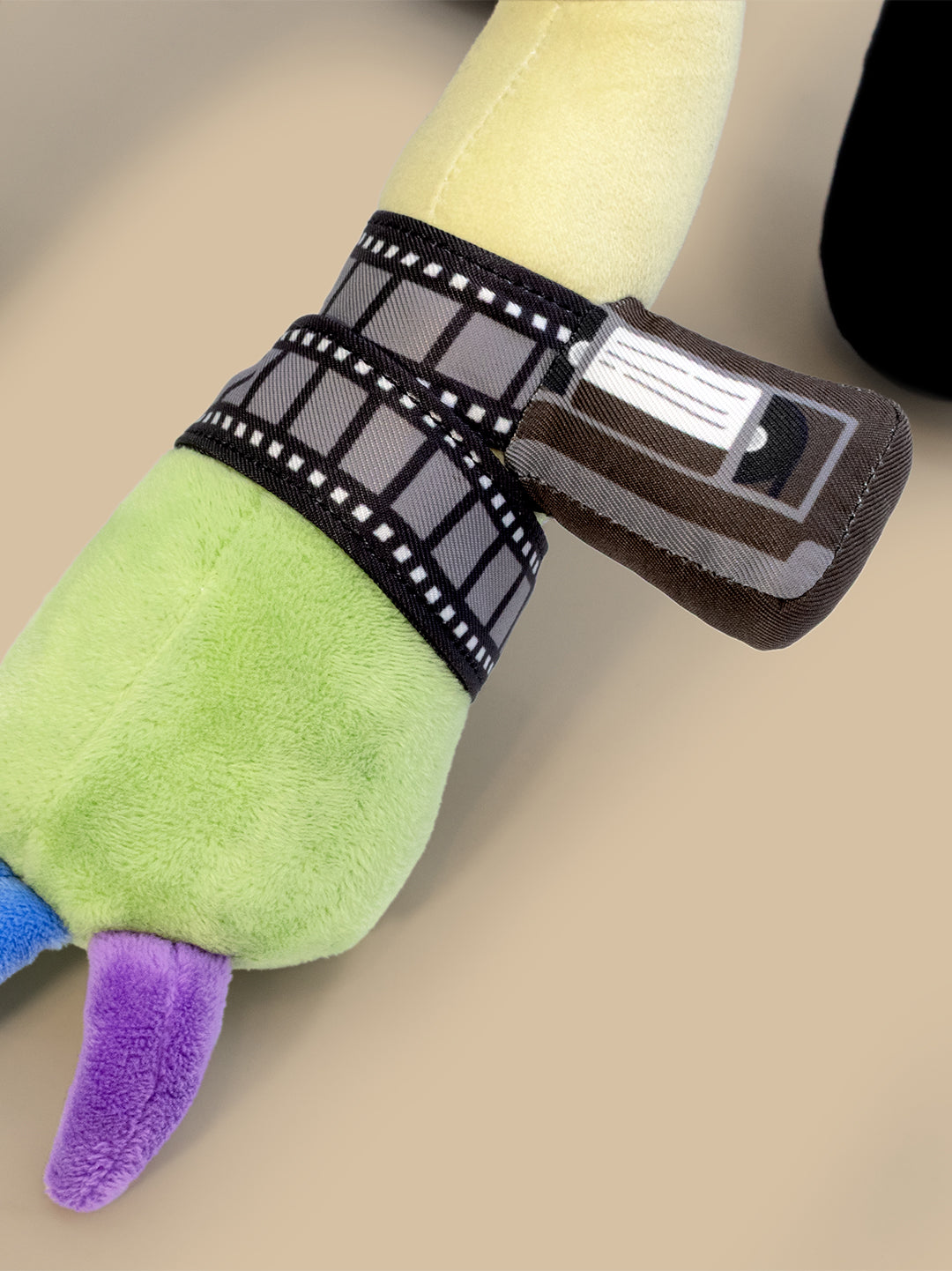 Close up of plush with tape reel around wrist on a beige surface