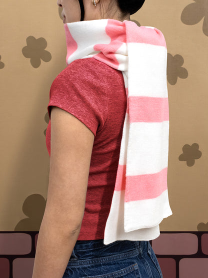 Person wearing a red shirt and striped scarf against a patterned wall.