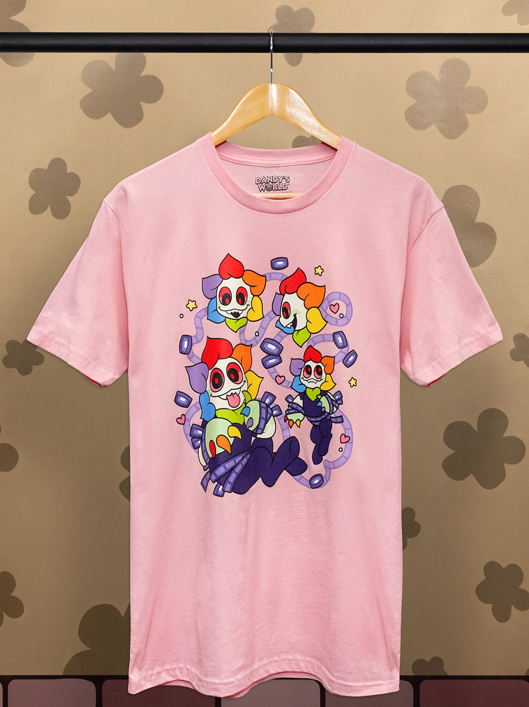 Pink t-shirt with colorful cartoon characters on a hanger against a patterned wall.
